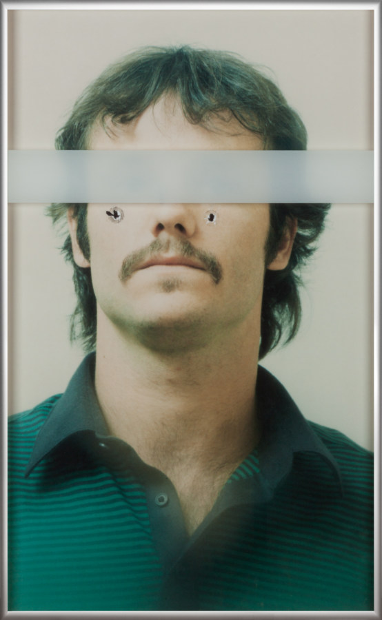 Framed color photograph of a mugshot with bullet holes and a thinly veiled white line over the eyes