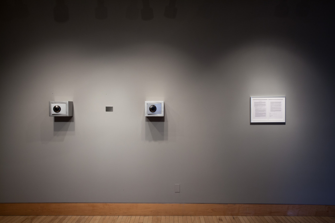 Color image of framed and sculptural works on grey gallery walls