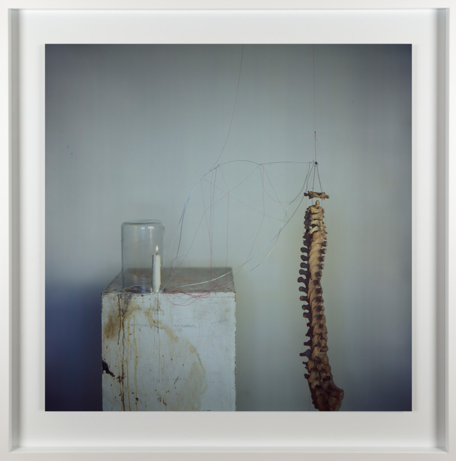 Color photograph of a lit candle and glass jar on a stone plinth next to a vertebrae