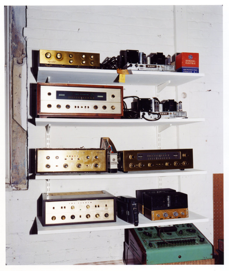 Color photograph of audio receivers on white shelves