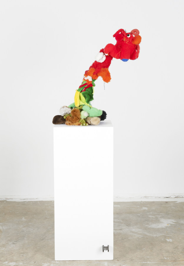 Color image of soft sculptural artwork made of plush toys leaning slightly on white pedestal