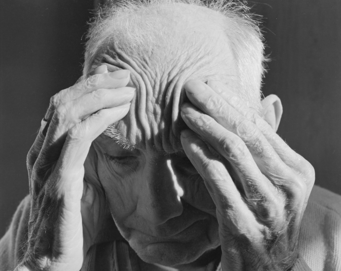 Black-and-white photograph of an old man pushing his fingers into his temples.