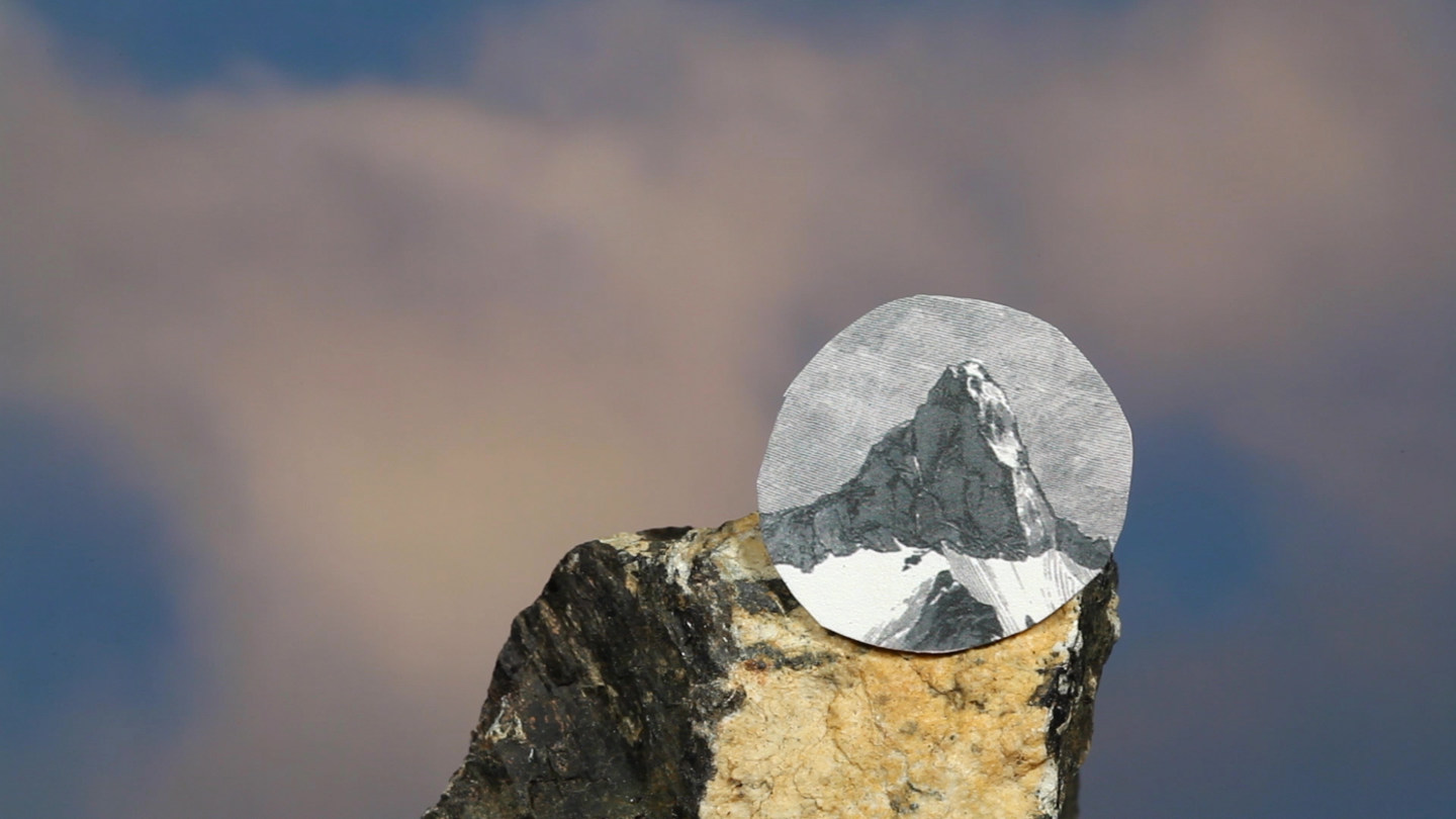 Color video still of a rock with a circular image of a mountain top