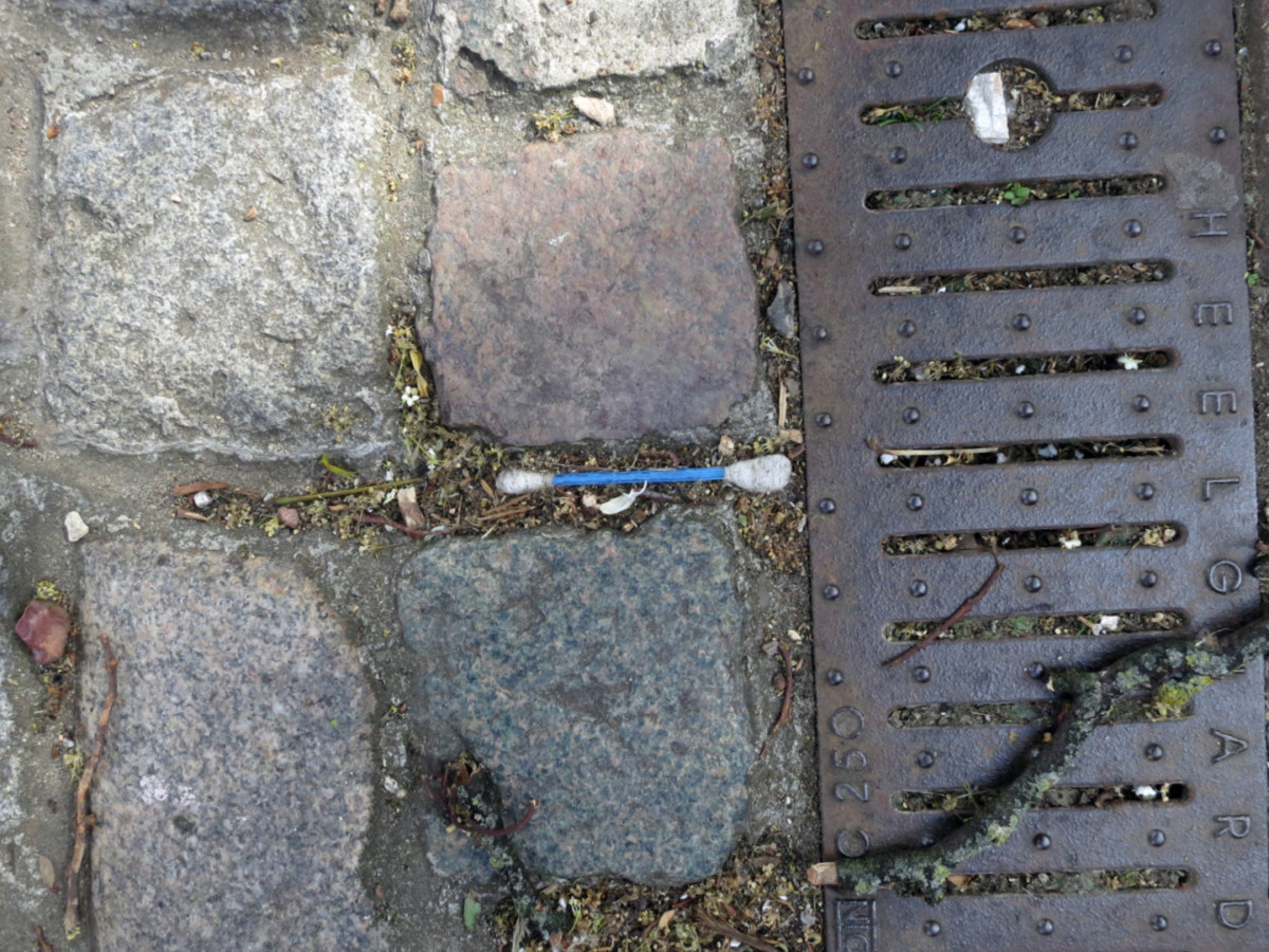 A photograph of a Q-tip on a brick sidewalk, stuck between two bricks