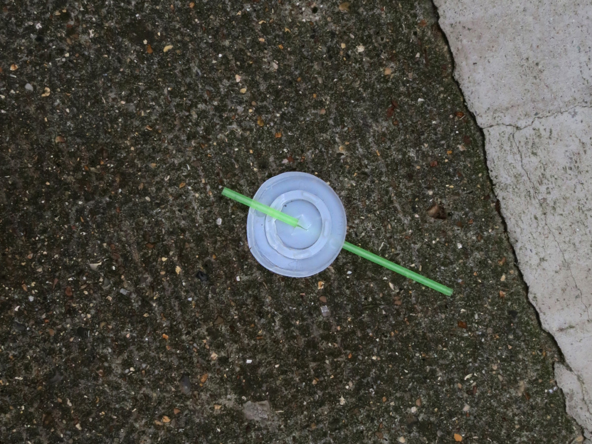A photograph of a disposable drink lid & green plastic straw in the street