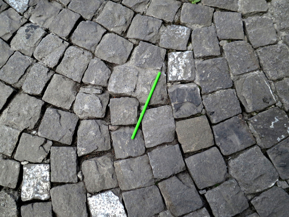 A photograph of a disposable green plastic straw on a cobblestone street