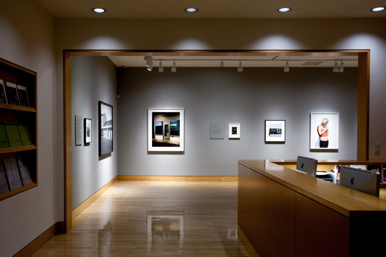 Color image of gallery entryway exhibiting color photographs of various sizes on grey gallery walls