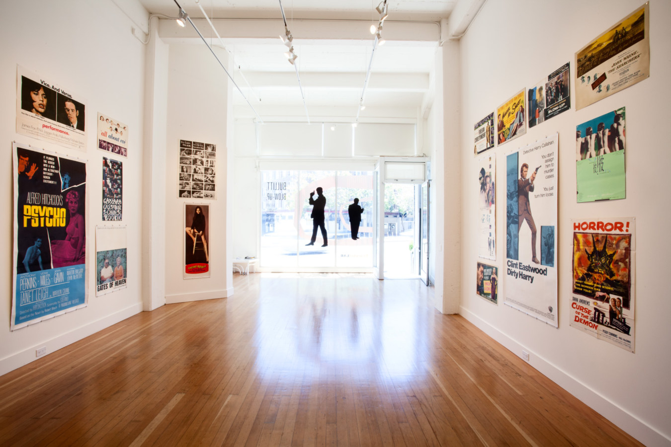 Color image of white walled gallery exhibiting various sized movie posters