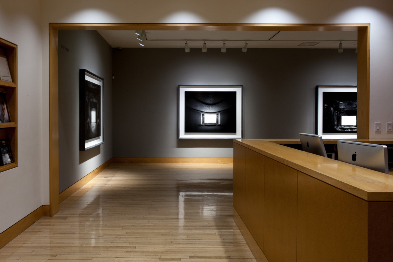 Color image of gallery entryway exhibiting large scale black and white photographs on grey gallery walls