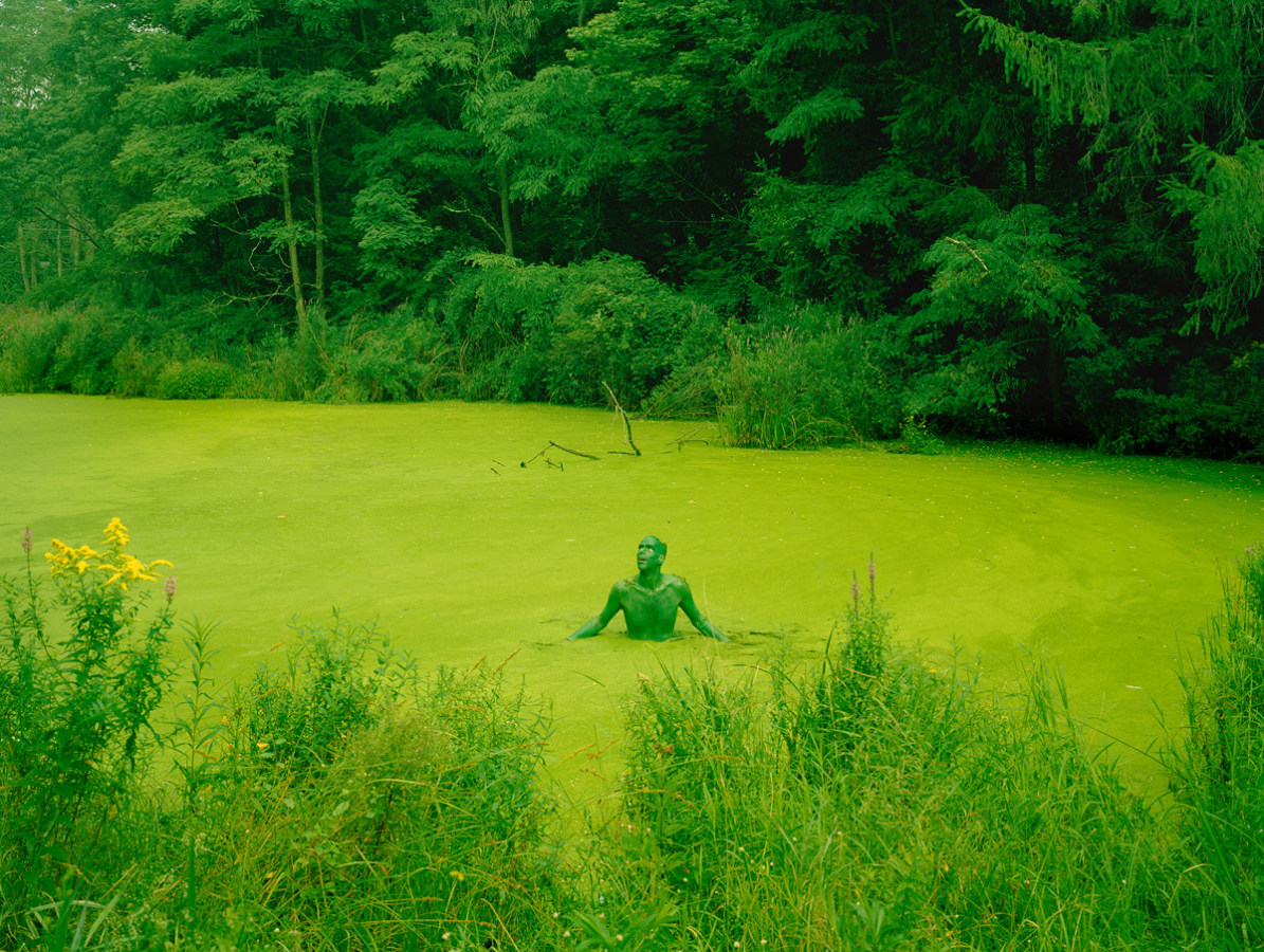 Color photograph of a green figure in a green mossy swamp