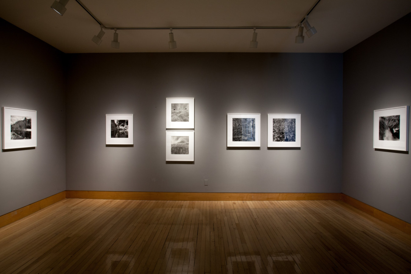 Color image of gallery entryway exhibiting black and white framed on grey gallery walls