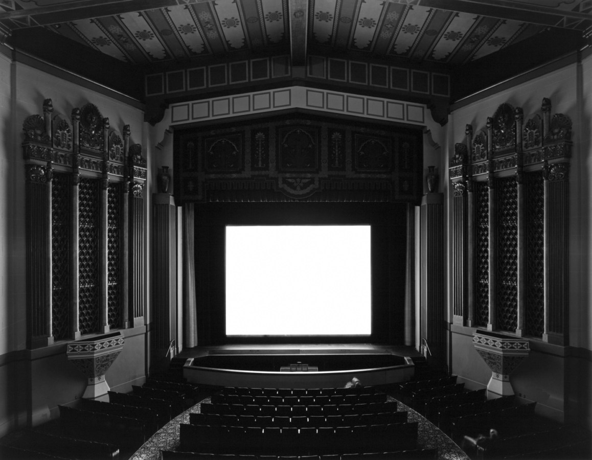 Black and white photograph of an empty theater with a large white screen
