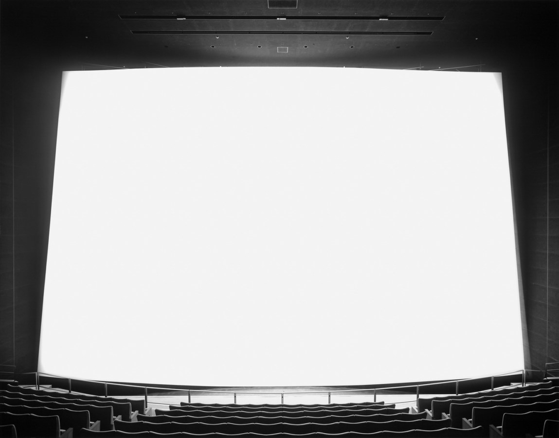 Black and white photograph of an empty theater with a large white screen