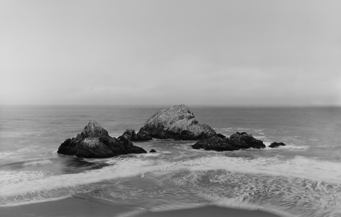 Black and white horizontal photograph of a rock formation in the Pacific Ocean