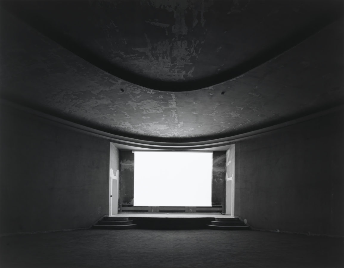 Black-and-white photograph of an empty theater with a glowing blank white screen