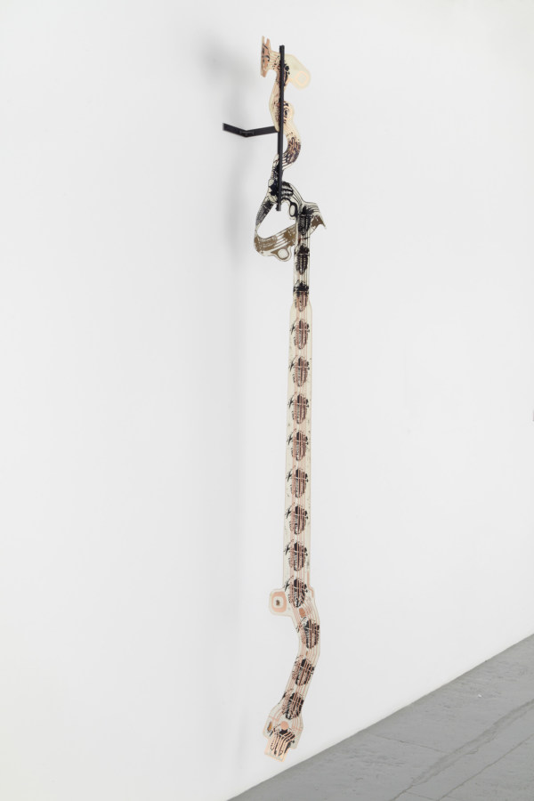 Color image of mixed media sculptural work hanging on wall dangling to floor depicting grenades on cooper-clad plastic