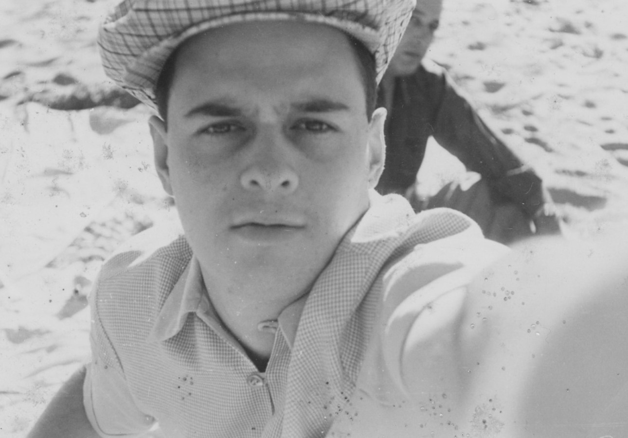Black and white selfie photograph of a white man in a button-up shirt and cap.