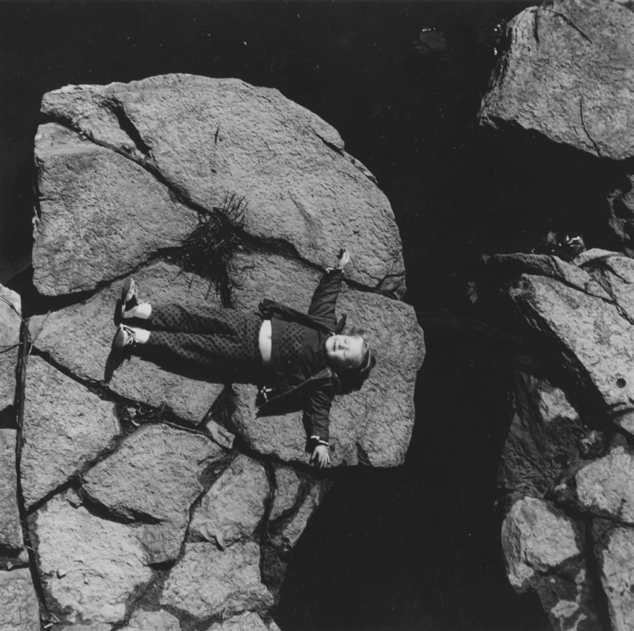 Black-and-white photograph of smiling small girl laying on a boulder.