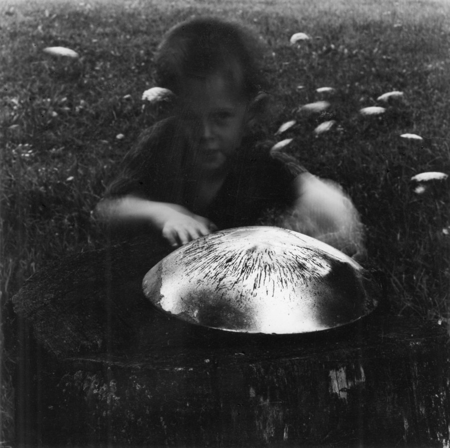 Black and white photograph of a young boy crouching behind a hubcap