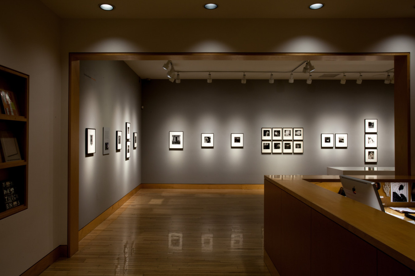 Color image of gallery entryway exhibiting black and white photographs on grey gallery walls