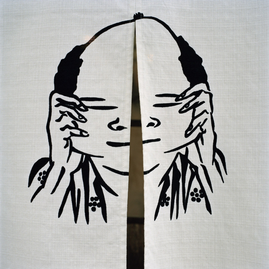 Color photograph of a painted face pulling cheeks on white fabric doors