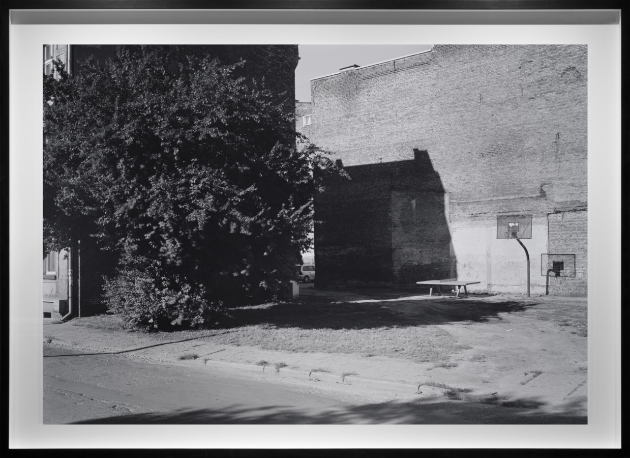 Black-and-white photograph of an empty basketball court against a the side of a bare brick building