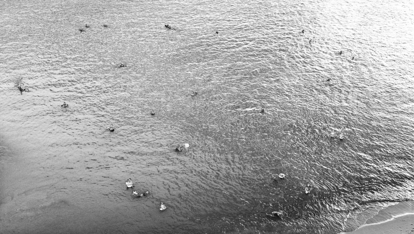 Black-and-white photograph of scattered swimmers in a calm ocean near the shore