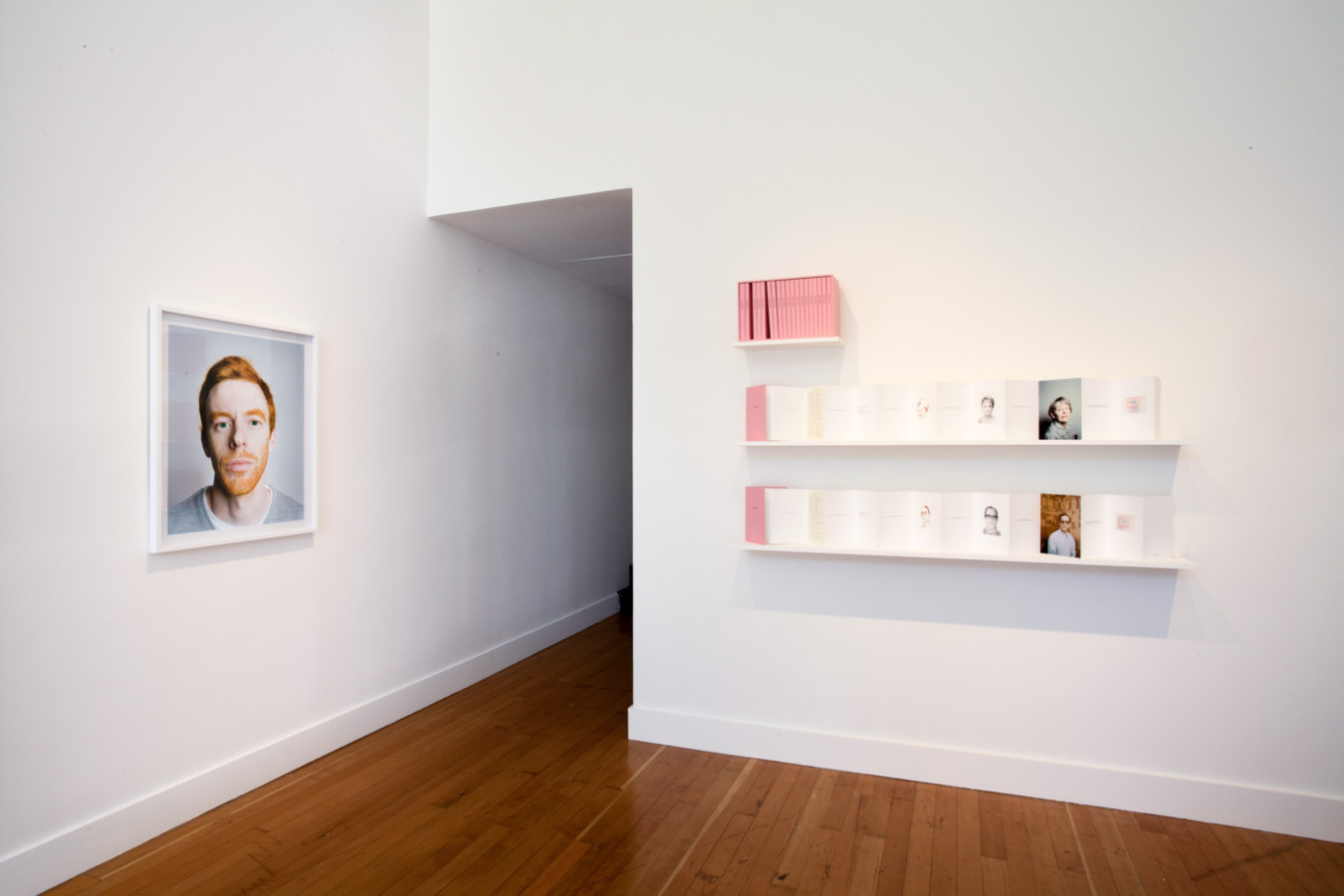 Color image of white walled gallery exhibiting framed artworks and printed publications