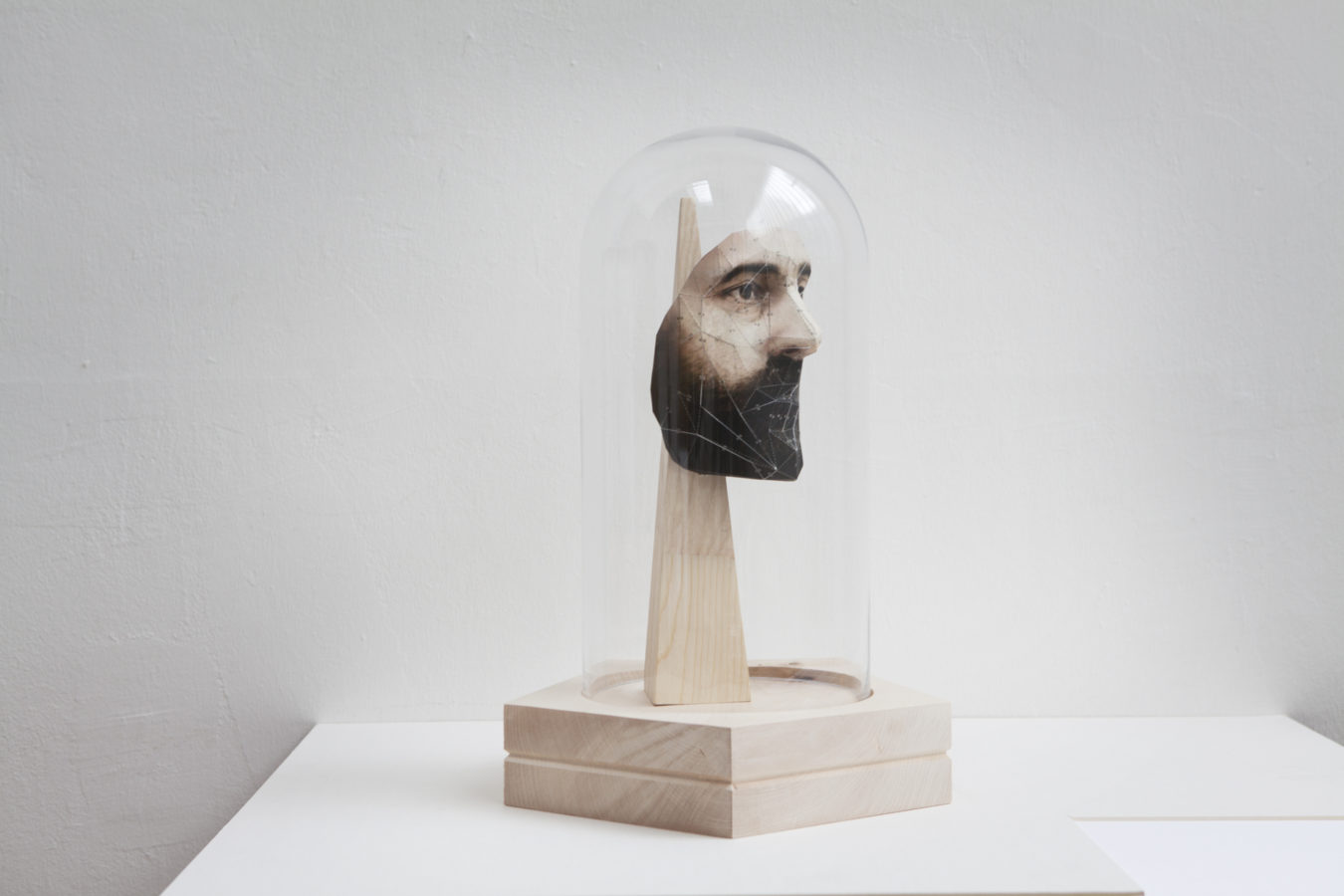 Color image of paper sculpture depicting a bearded mans face encased on wooden stand and encased in glass