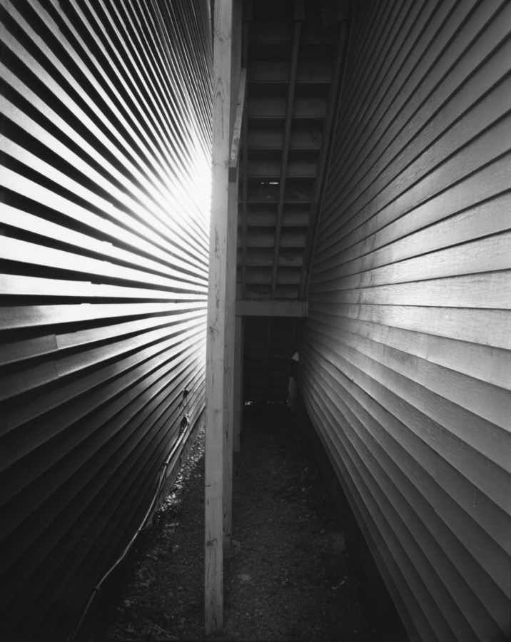 Black-and-white photograph of a stairway from beneath between two clapboard walls