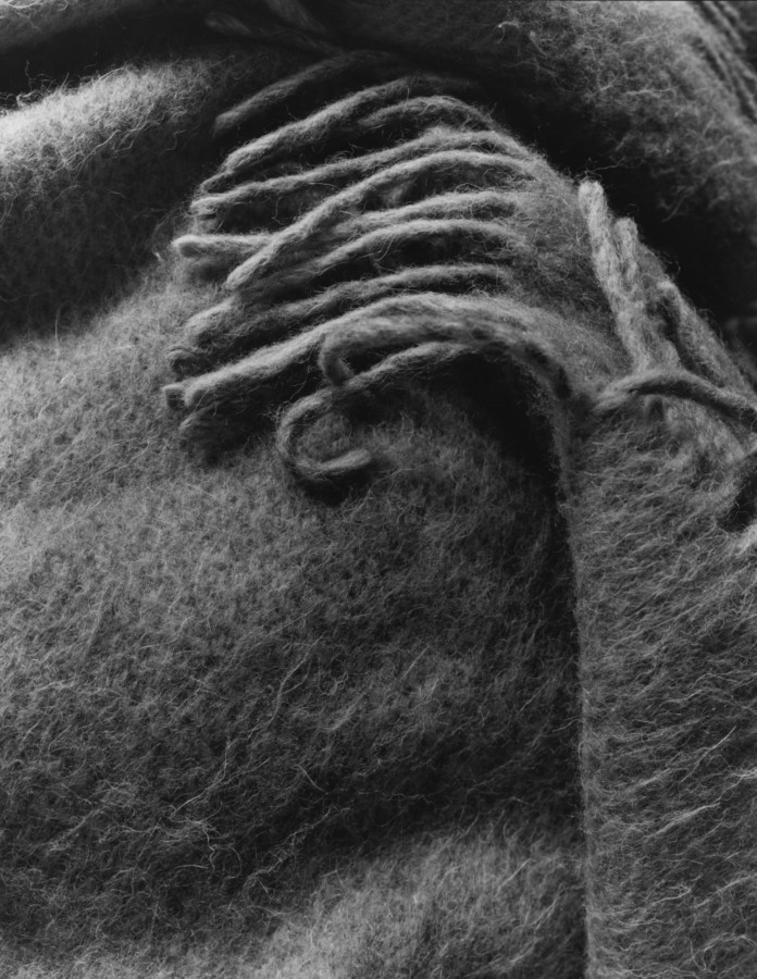 Black-and-white photograph of the corner of a wool shawl with fringed edges