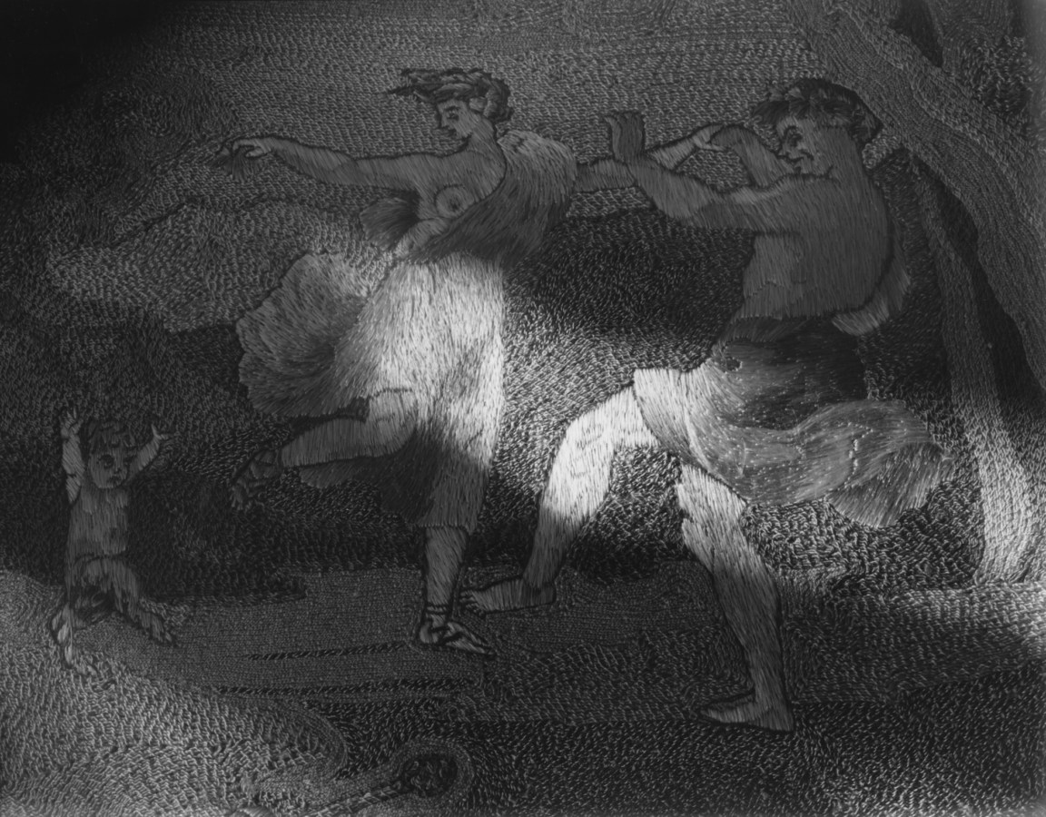 Black-and-white photograph of a patch of light on an embroidered picture of two dancing figures and a satyr