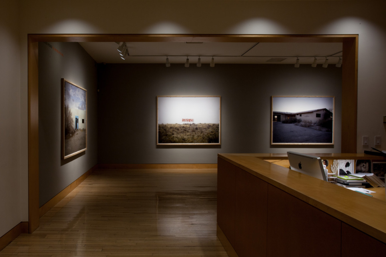 Color image of gallery entryway exhibiting large scale color photographs on grey gallery walls