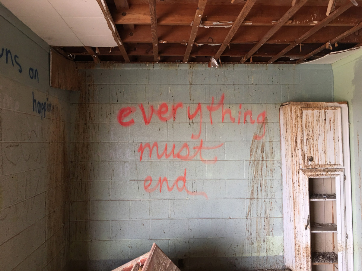 Color photograph of fluorescent red spray-painted writing on an interior cinderblock wall of an abandoned building