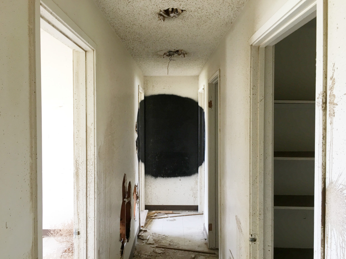 Color photograph of a black spray-painted circle at the end of a white hallway of an abandoned building