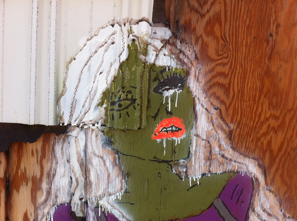 Color photograph of a painting of a woman with green skin on a wooden wall