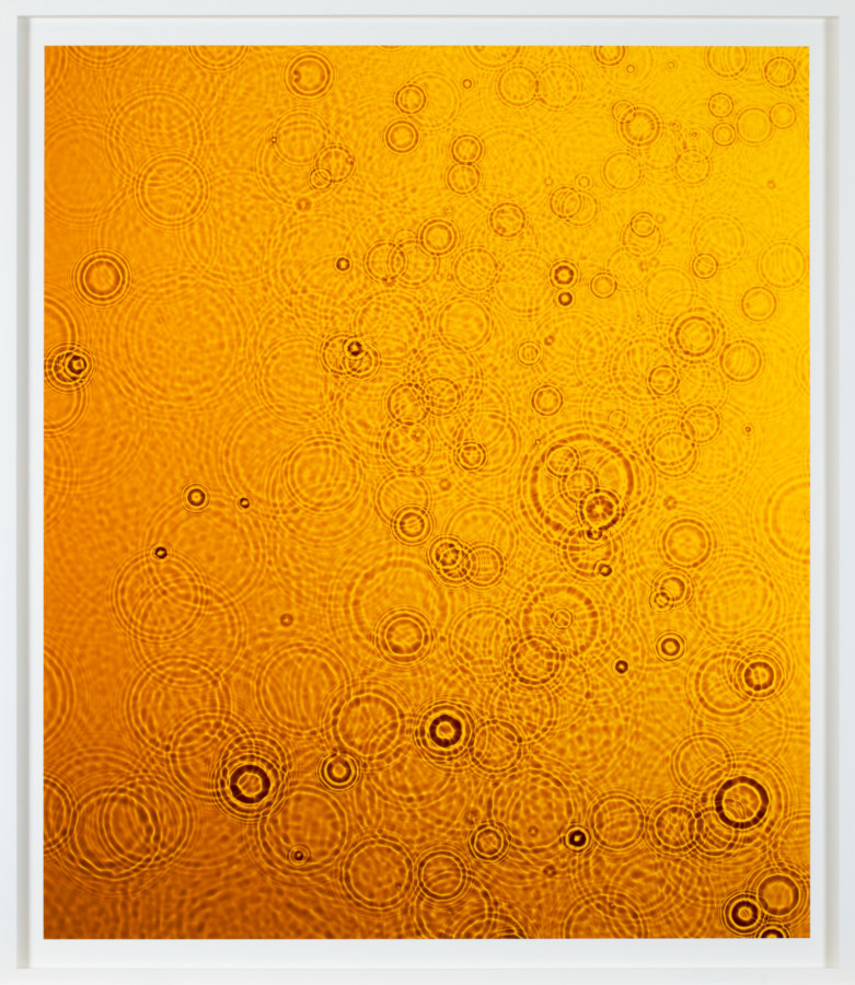Color image of white framed photograph depicting water ripples hued in a yellowish orange