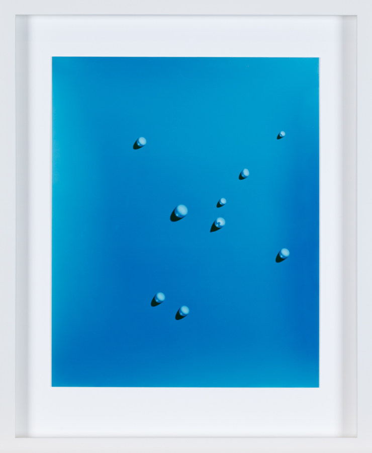 Color image of white framed photograph depicting water droplets on blue background