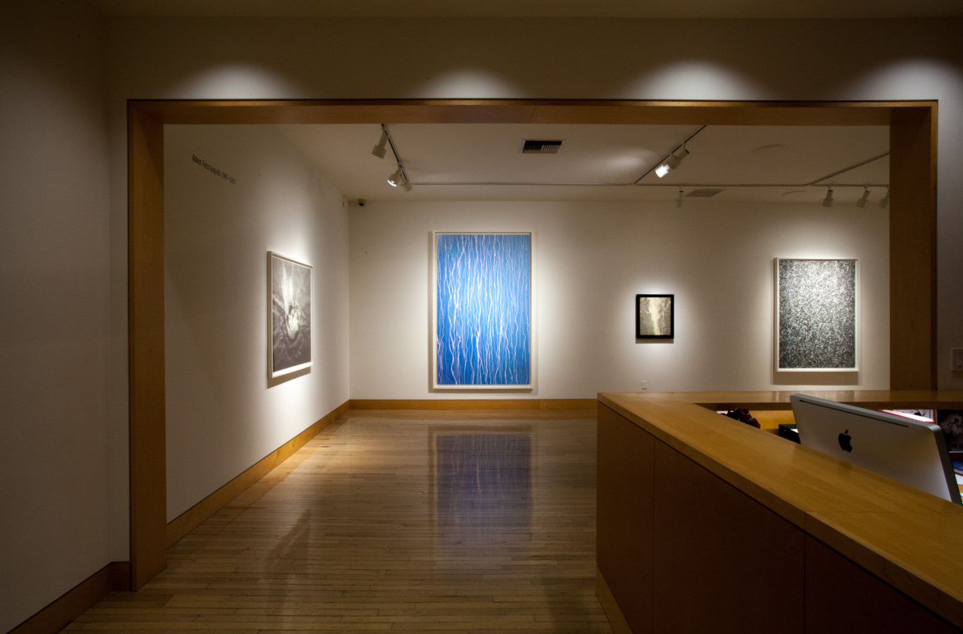 Color image of gallery entryway exhibiting large scale color photographs on white gallery walls