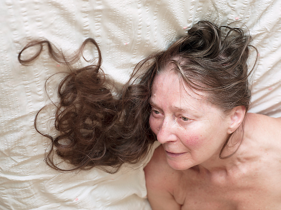 Color photograph of a woman laying down, her hair arranged in curls on the bedsheet.