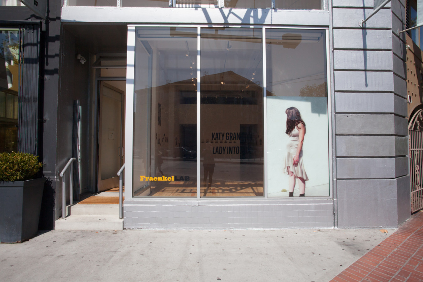 Color photograph of a gallery exterior with decal depicting a women in a dress with face covered with hair