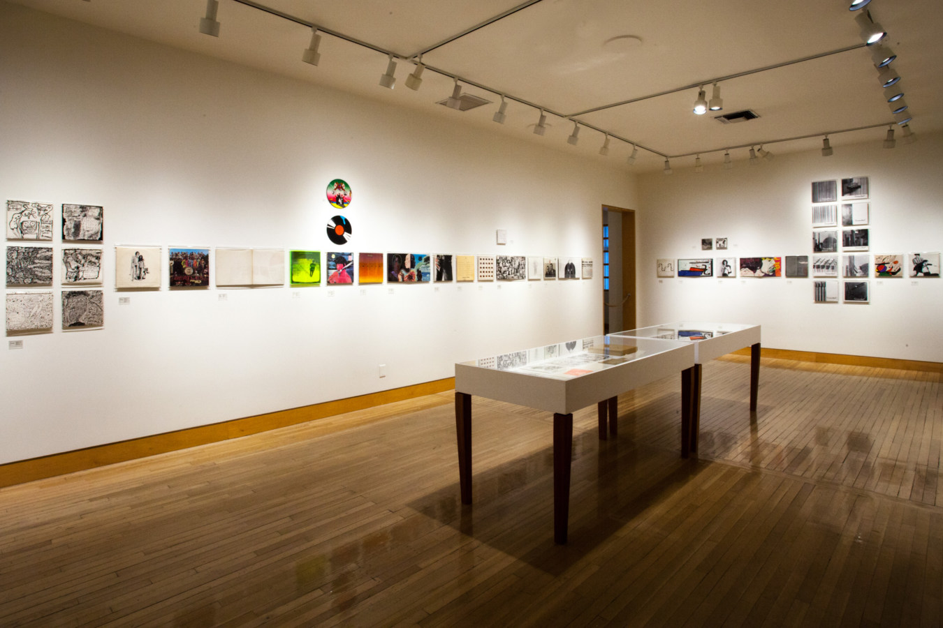 Color image of vinyl records and record sleeves inside white vitrine and on white gallery walls