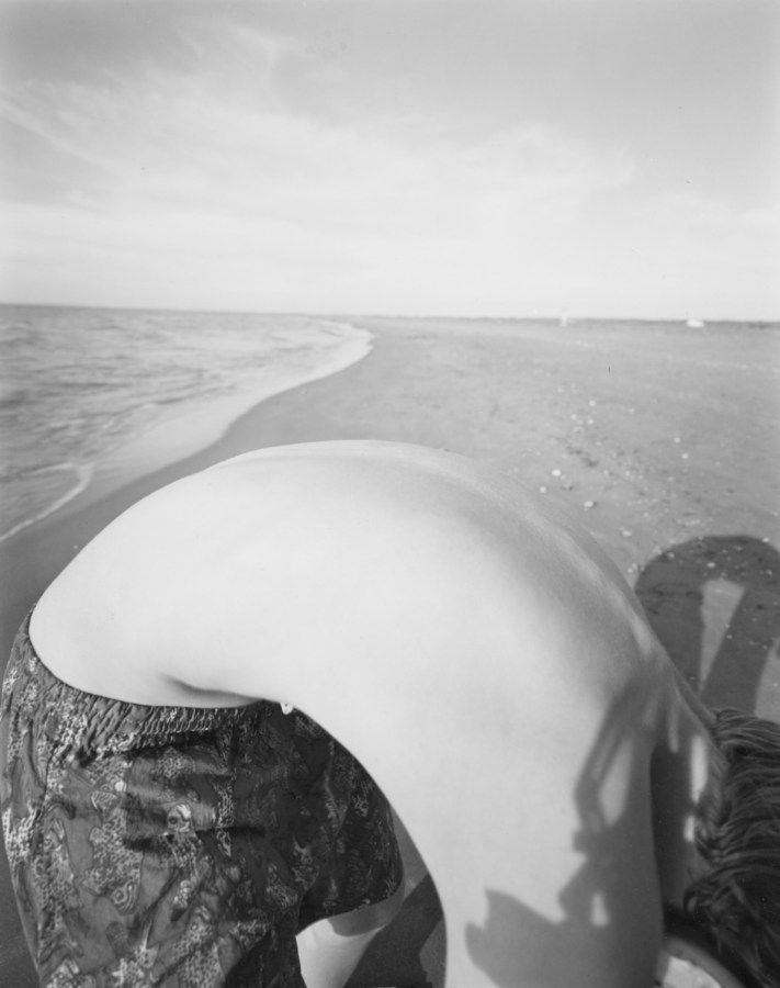 Black-and-white photograph of of a boy's bent-over back against the backdrop of a seashore