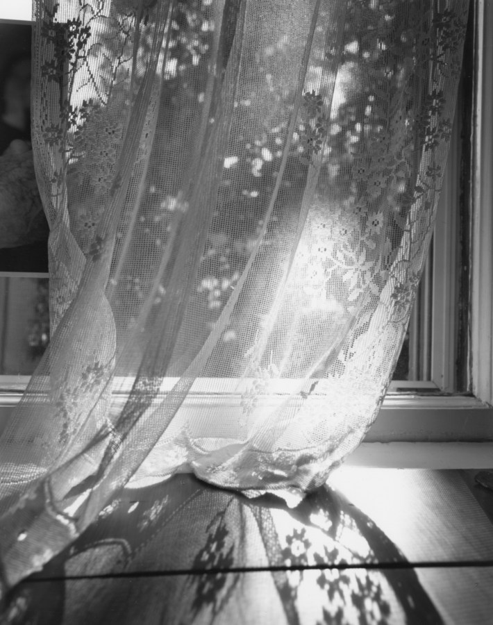 Black and white photograph of sunlight filtering through a lace curtain