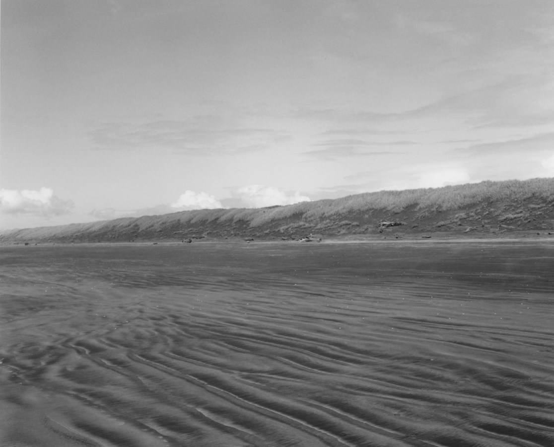 Black-and-white photograph of a beach with scattered clouds on the horizon.