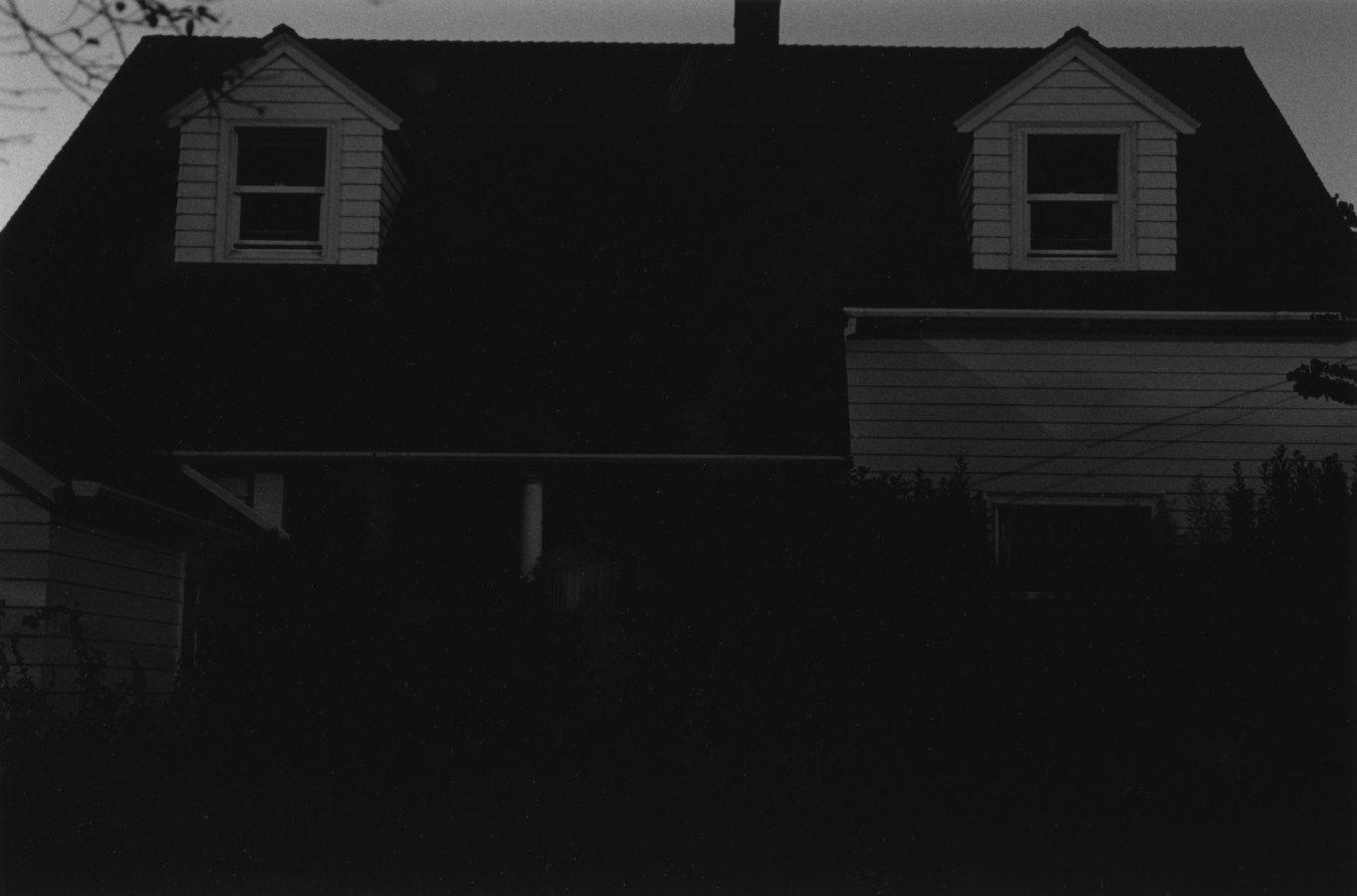 black-and-white vertical photo of a dimly lit house with two dormers