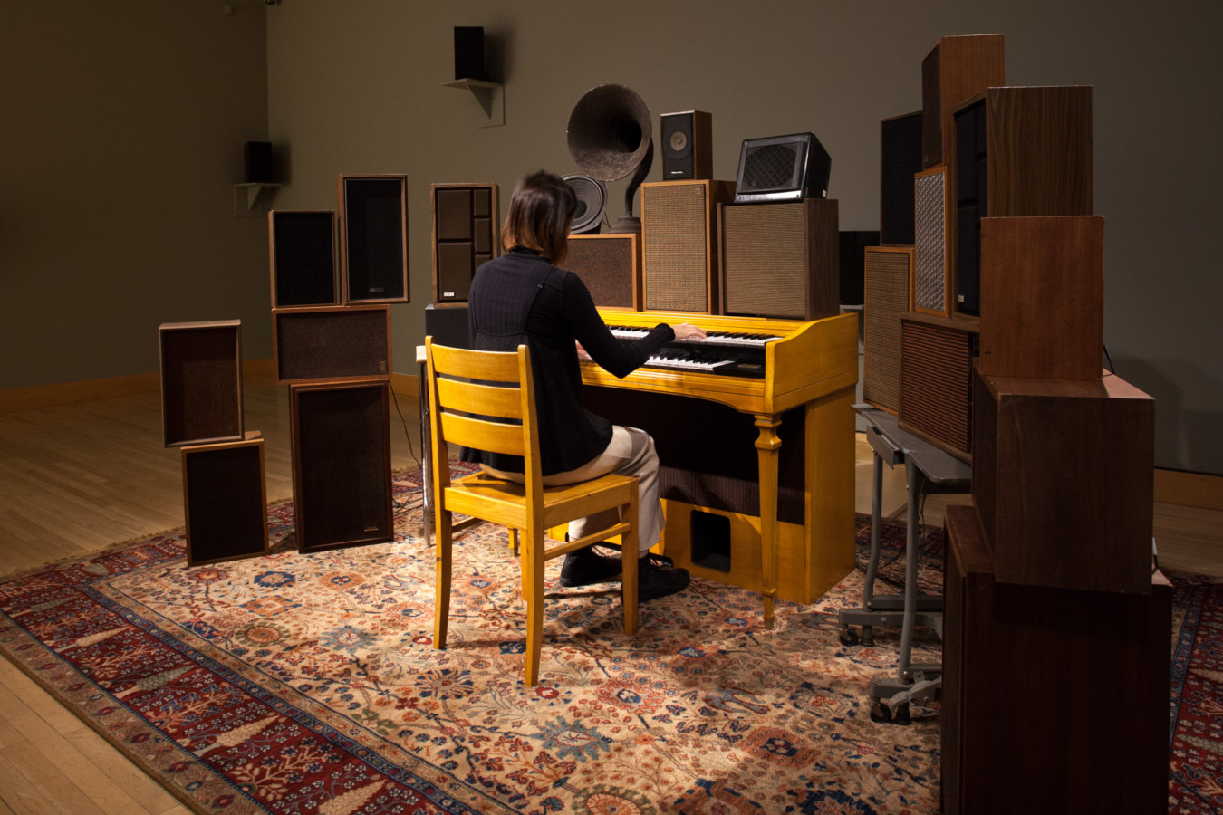 Color image of a person playing an organ surrounded by speakers of various sizes and vintages on an ornate carpet