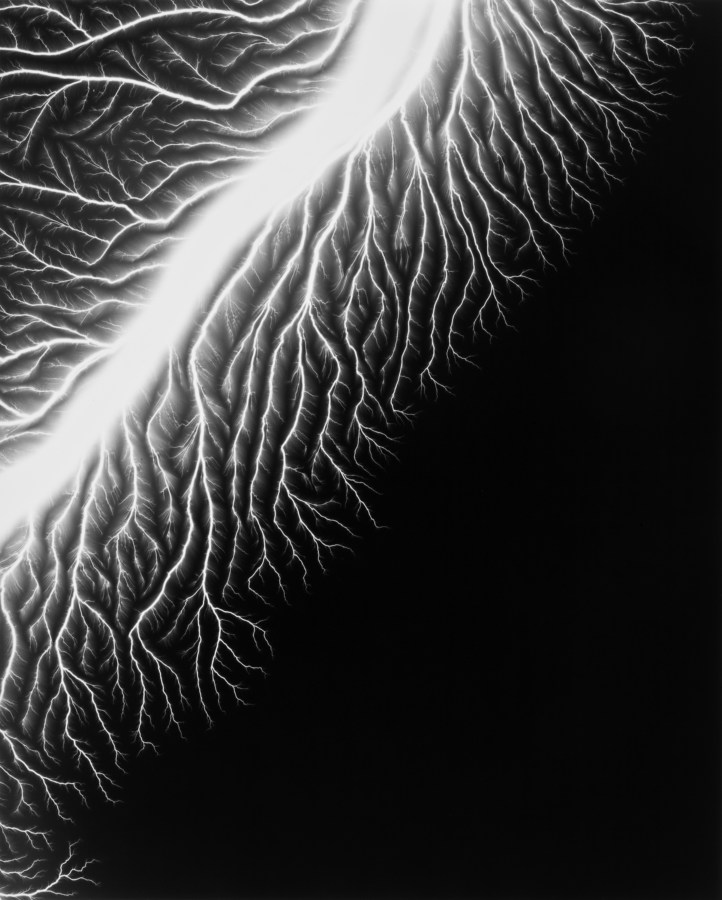 Black-and-white photograph of a white trail of light in the top left corner with smaller branches coming off of it on a black background