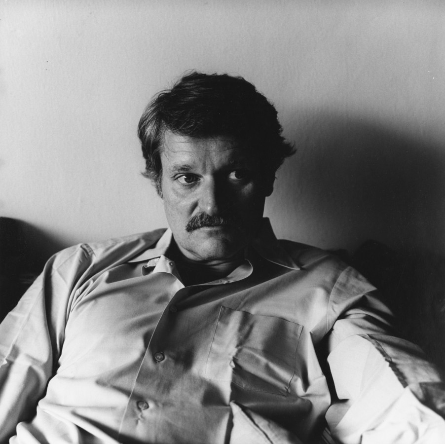 Black and white photograph of mustachioed man in white button looking off