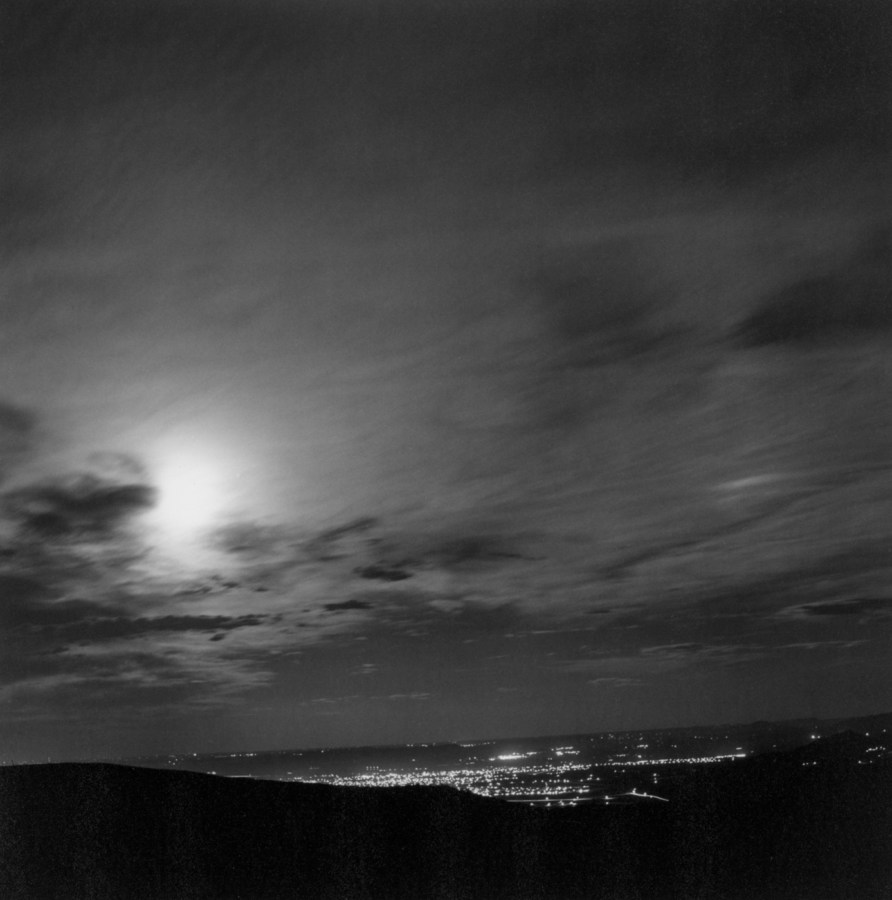 Black-and-white photograph of city lights in the distance at night